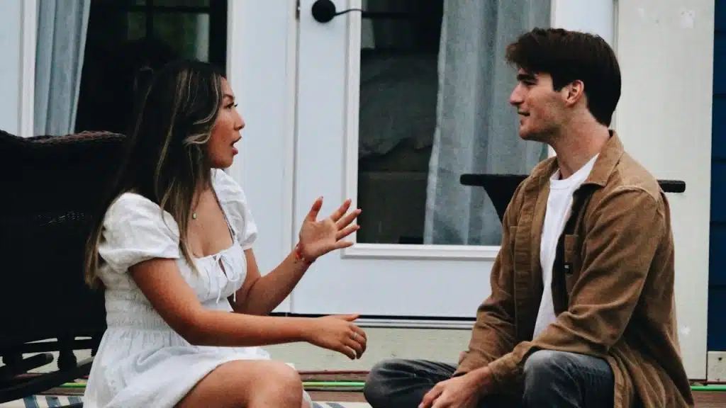 A woman talking to a man as they sit on the outside stairs of their house.