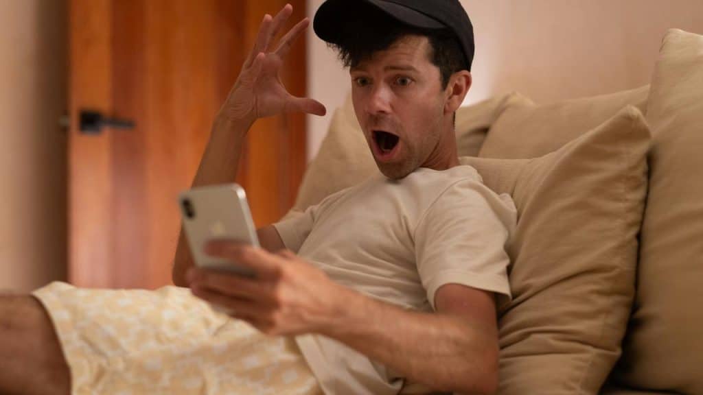 A man is surprised and is lying on a couch, looking at something on his phone.