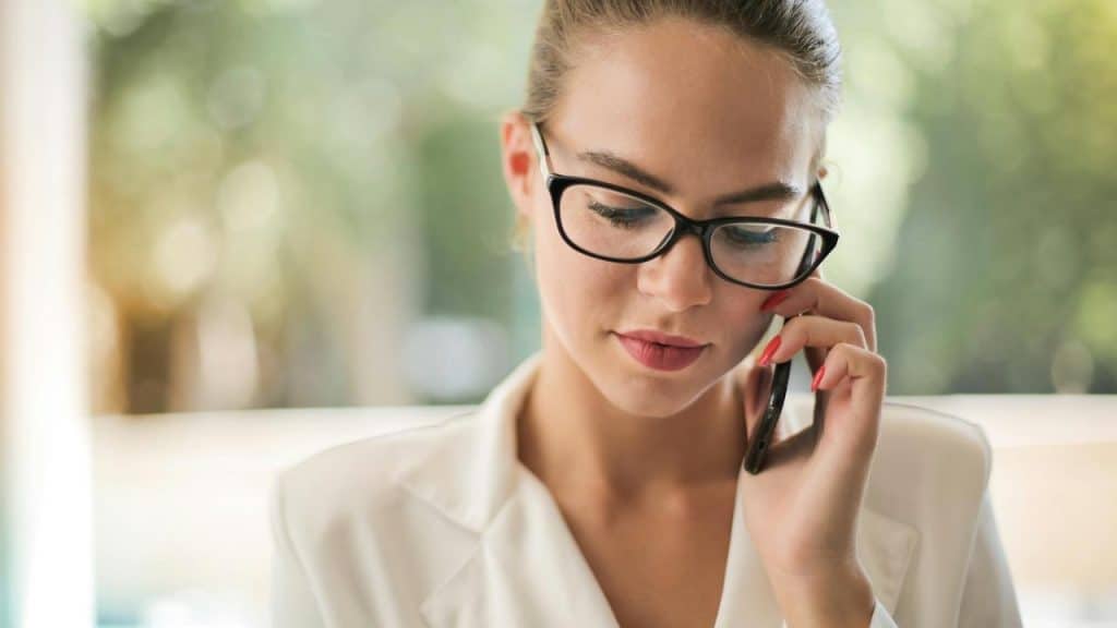 A woman with glasses and a mobile phone talking inside.