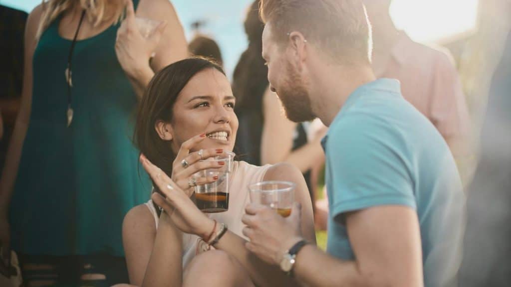 A woman and man smiling and talking while holding drinks at a social gathering.