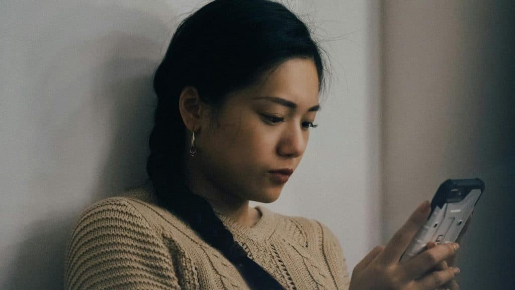 A woman with her arm resting on a wall, gazing at her cell phone.