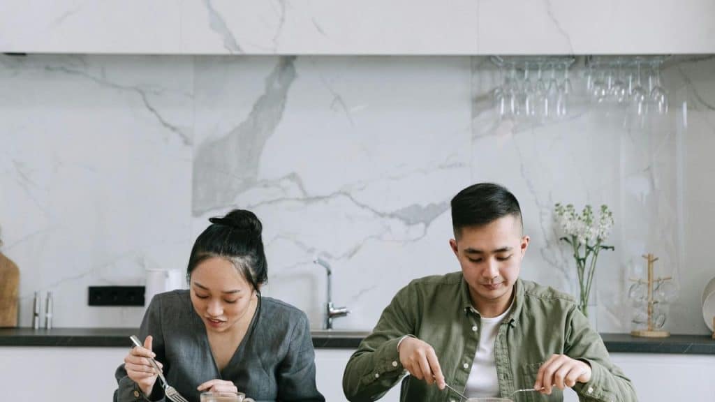 A man and a woman seated at a counter, eating a meal together.