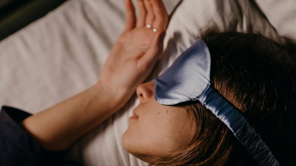 Person sleeping in bed with blue sleep mask.