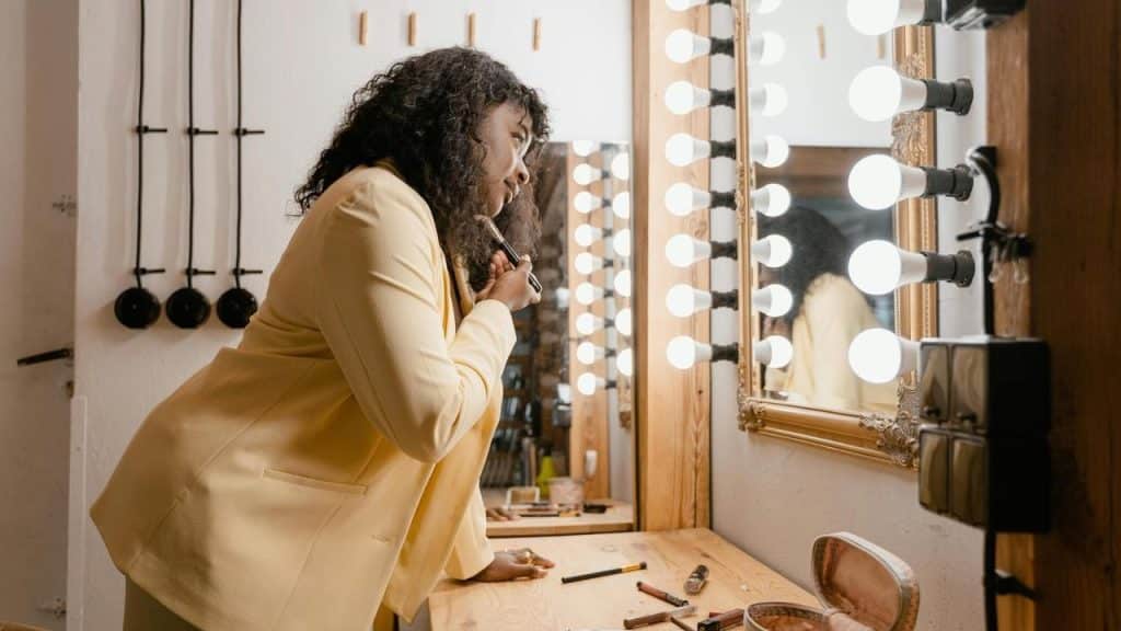 A woman putting on her makeup in front of a lighted mirror.