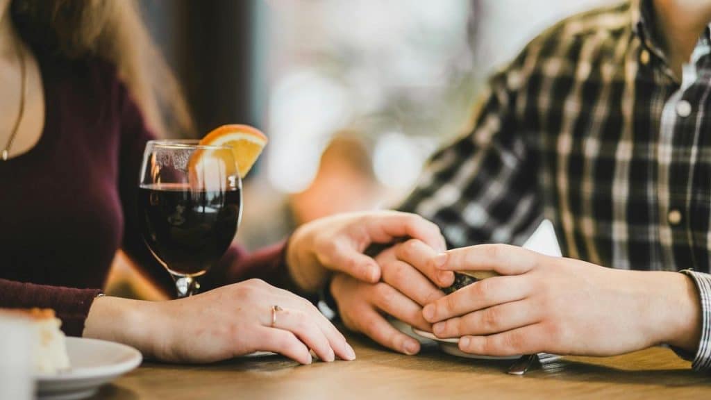 A couple holding hands at a table, next to a glass of wine.