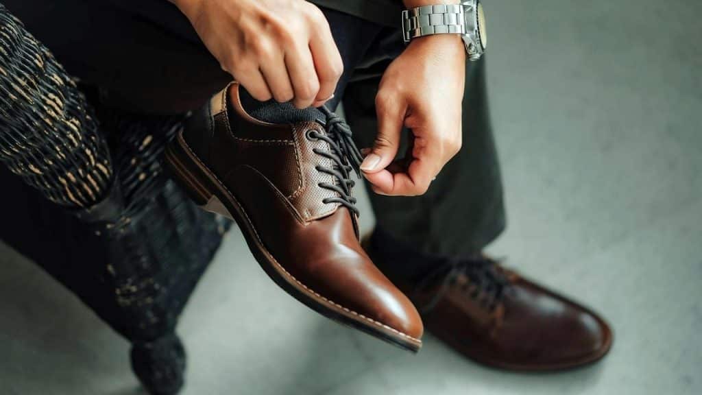 A man who is lacing a brown dress shoe.