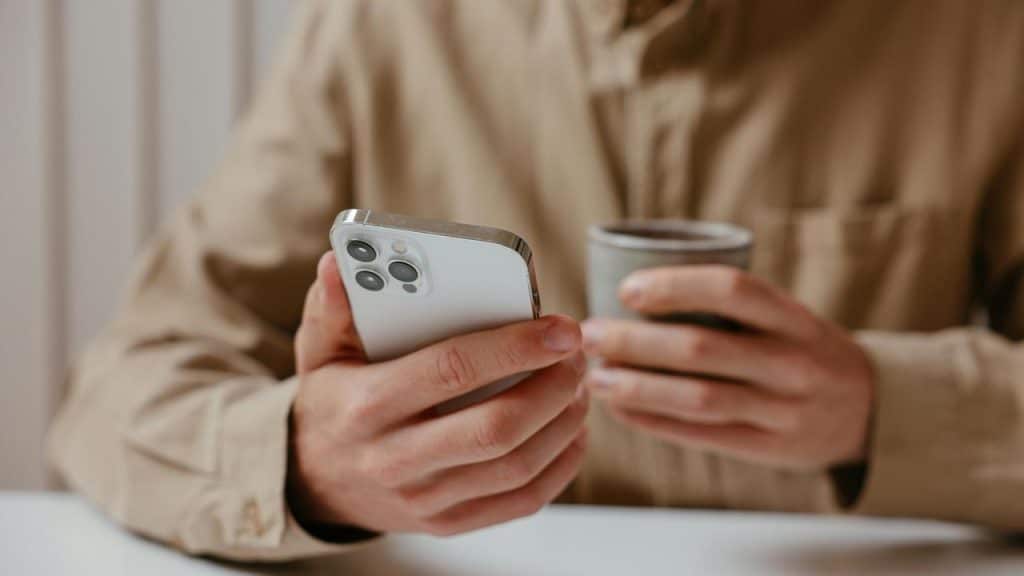 A man with his hands on a smartphone and coffee.