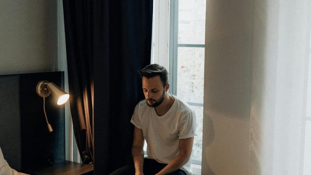 A man sitting quietly by a window in a dimly lit room.
