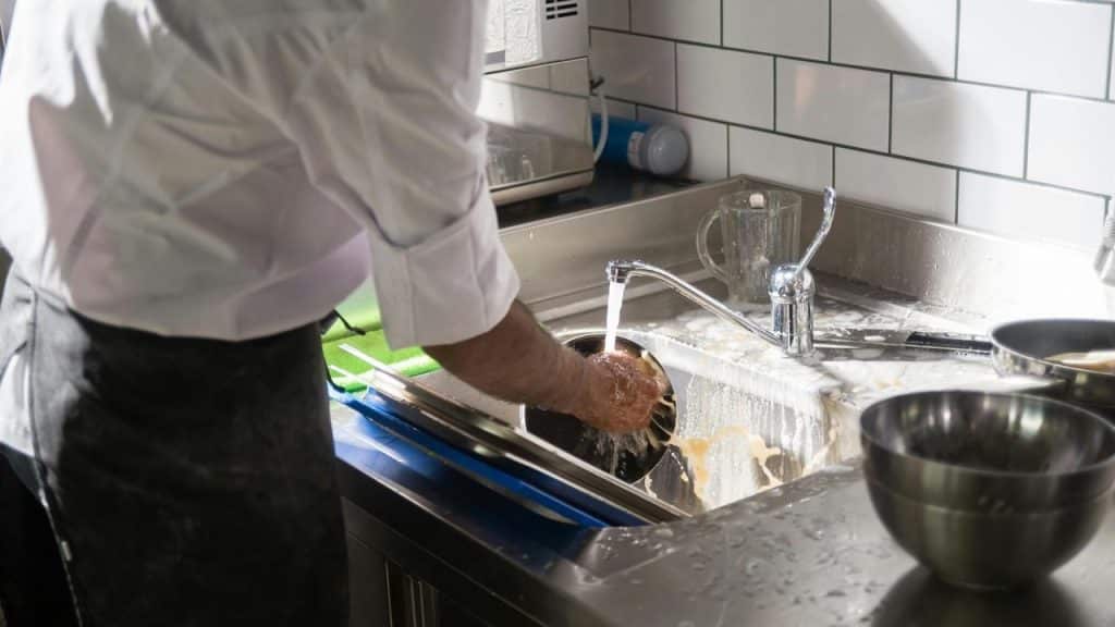 A man is washing dishes in a kitchen sink.