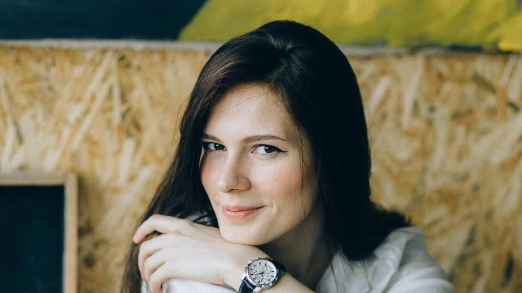 A woman with long dark hair resting her chin on her hand, smiling softly at the camera.