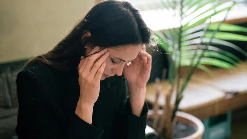 A woman holding her temples with her head down, appearing stressed.