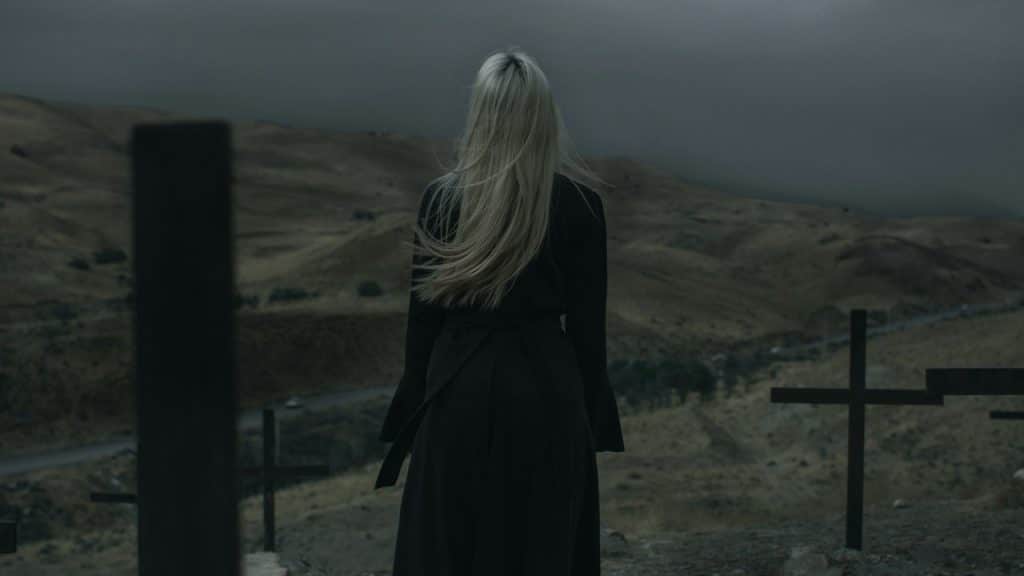 A woman standing amongst graves on a hill in the evening.