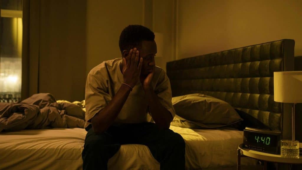 A man sitting on a bed at night looking stressed.