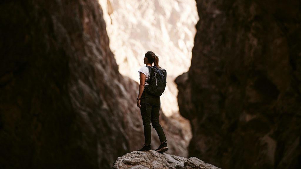 A woman with a backpack standing on a rock between two cliffs.