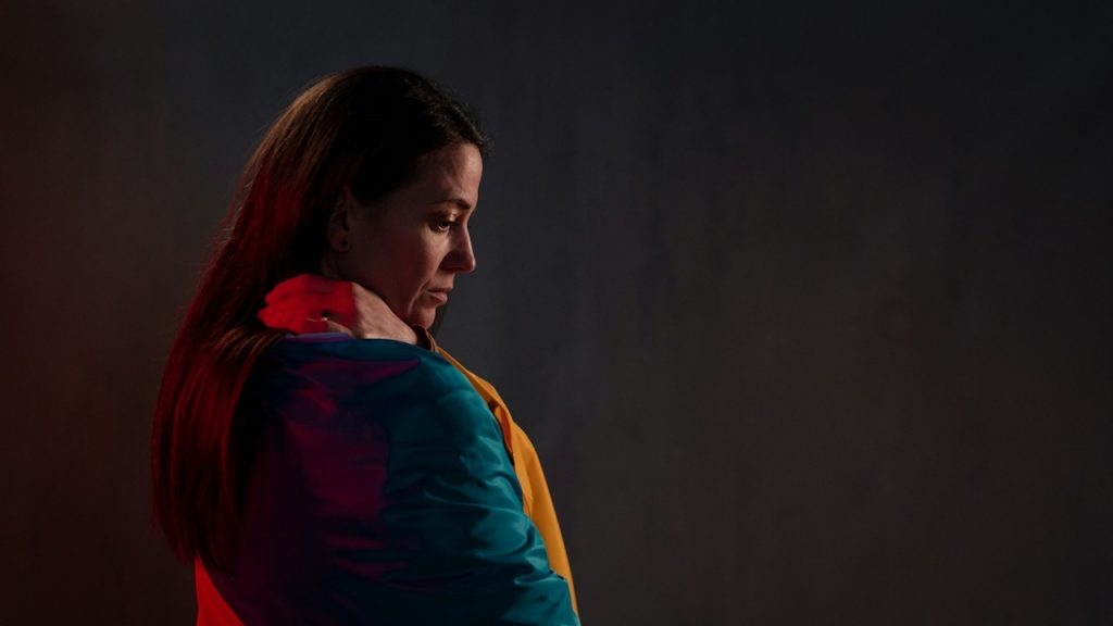 A woman looking downwards while standing in a dimly lit room.