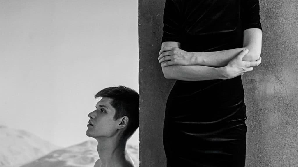 Closeup of a man sitting on the floor and a woman standing.