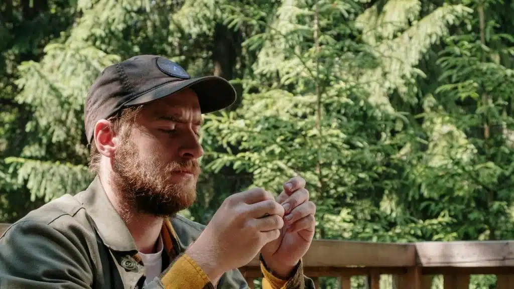 A man in a cap examining something closely while sitting outdoors.