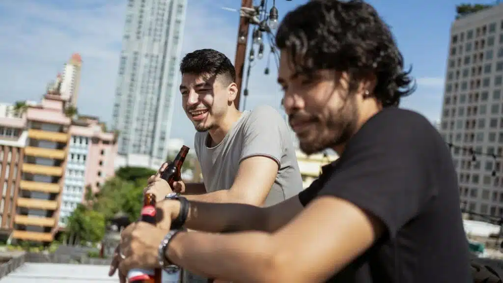 A pair of men relaxing with drinks on a rooftop overlooking a city.