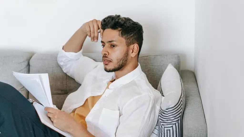 A man sitting on a couch reviewing papers with a thoughtful expression.