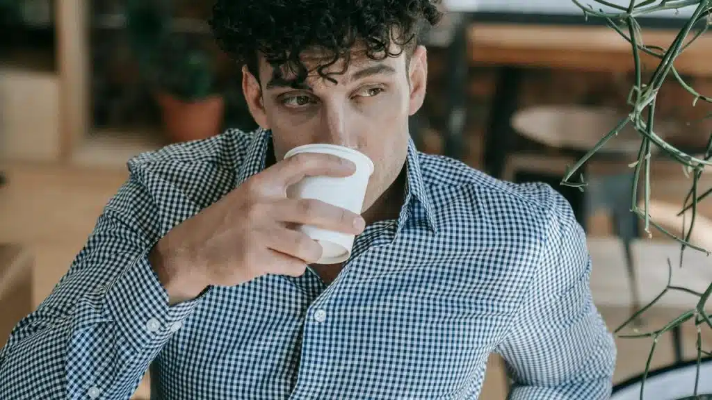 A man drinking from a cup while looking off to the side.