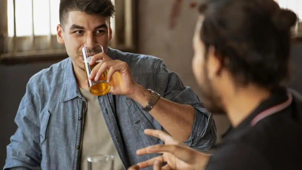 A man drinking from a glass while sitting and talking with another person.