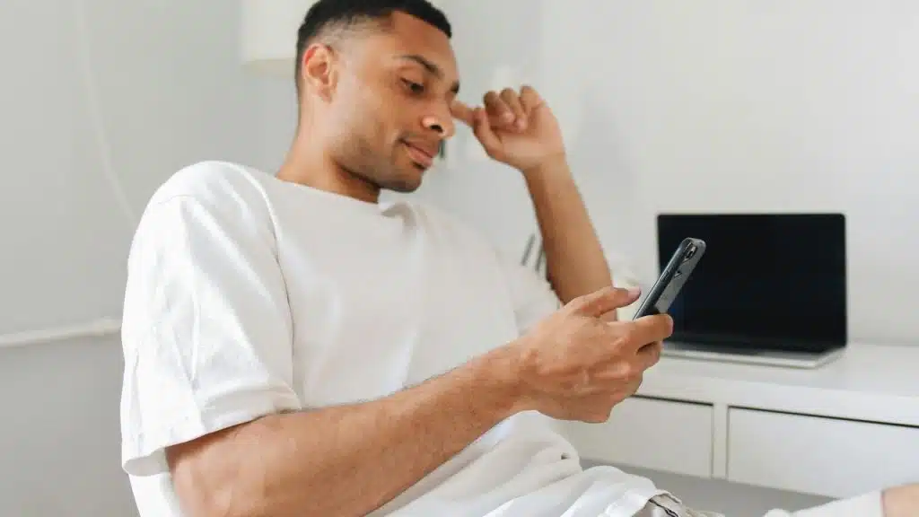 A man sitting and looking at his phone with a thoughtful expression.