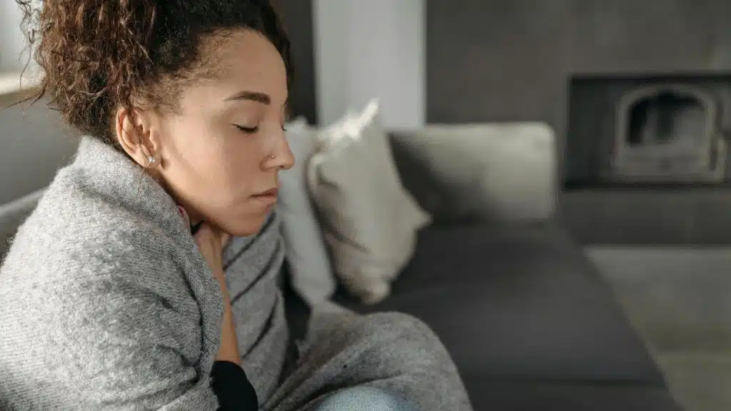 A woman wrapped in a blanket sitting on a couch with her eyes closed.