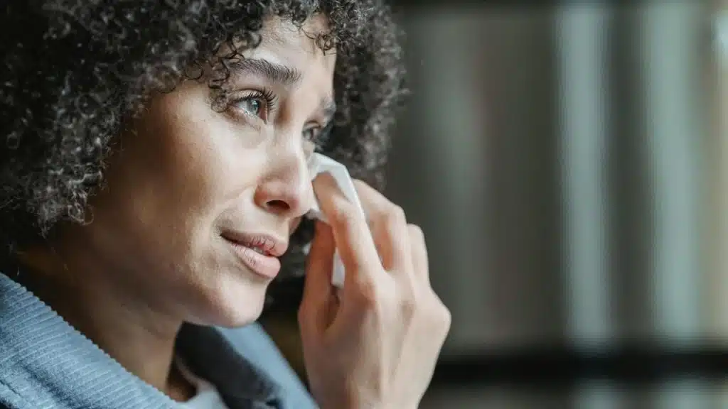 A woman holding a tissue to her eye with a tearful expression.