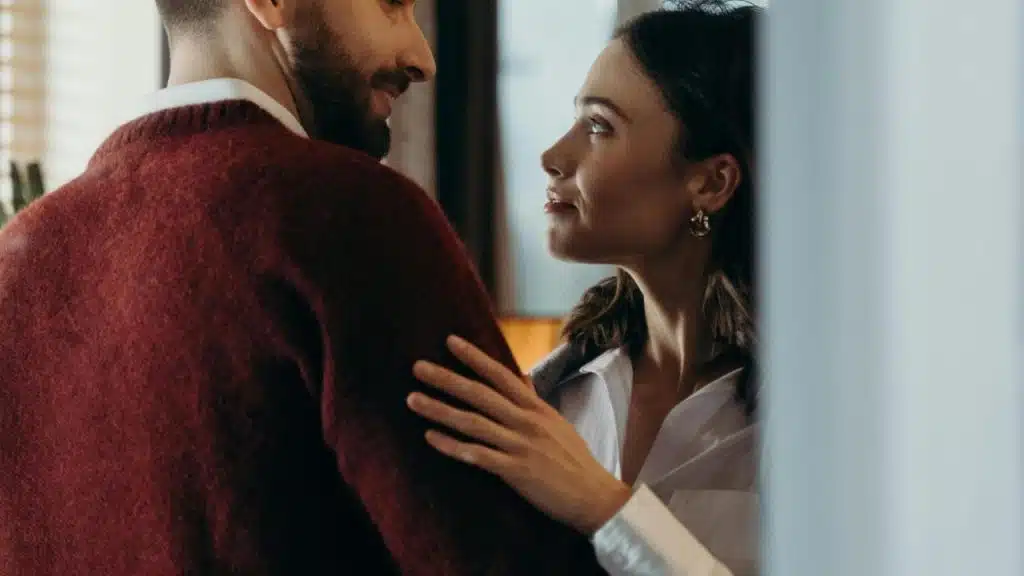 A woman and a man standing close together, facing each other indoors.