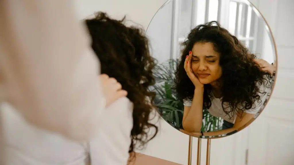 A woman looking at her reflection in a mirror with her hand on her face.