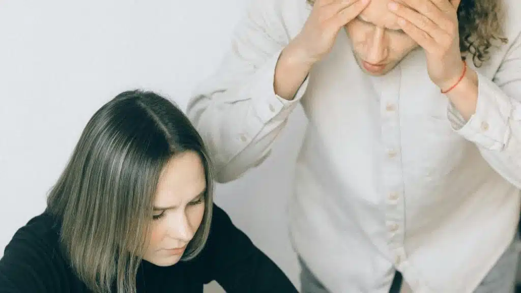A stressed couple with one person holding their head while the other looks down.