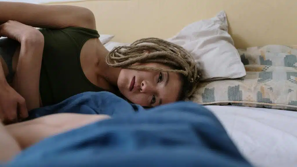 A person lying on a bed, looking tired and resting on a pillow.