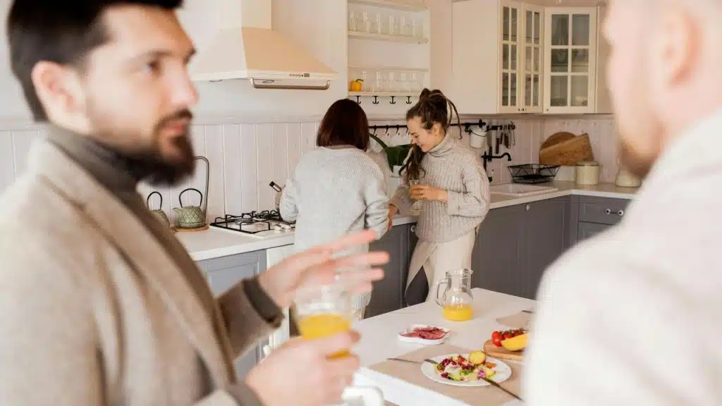A group in a kitchen, with two talking and two preparing food.