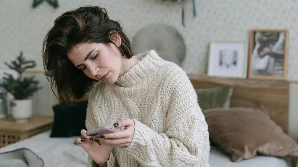 A woman looking down at her phone while sitting indoors.
