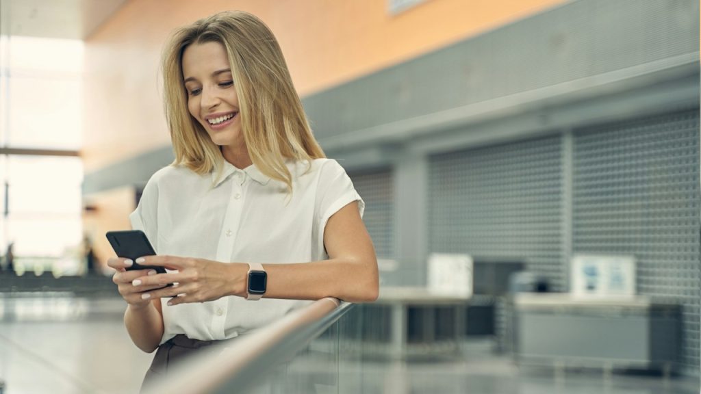 A woman smiling while texting on her phone.