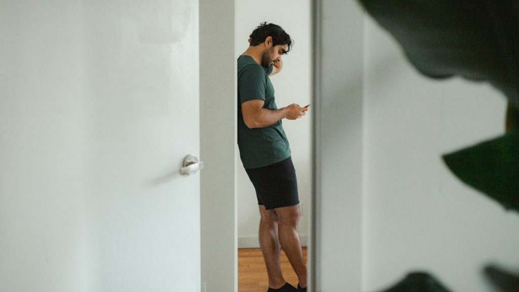 A man leaning on a wall while using his cellphone.