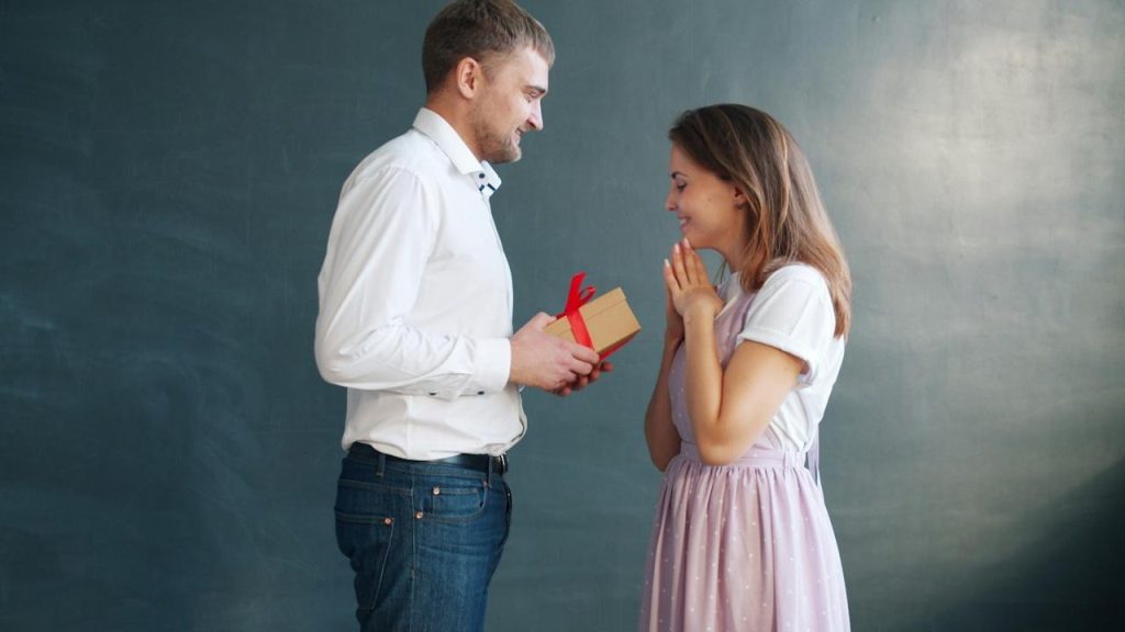 A man gives a woman a gift with surprised joy.