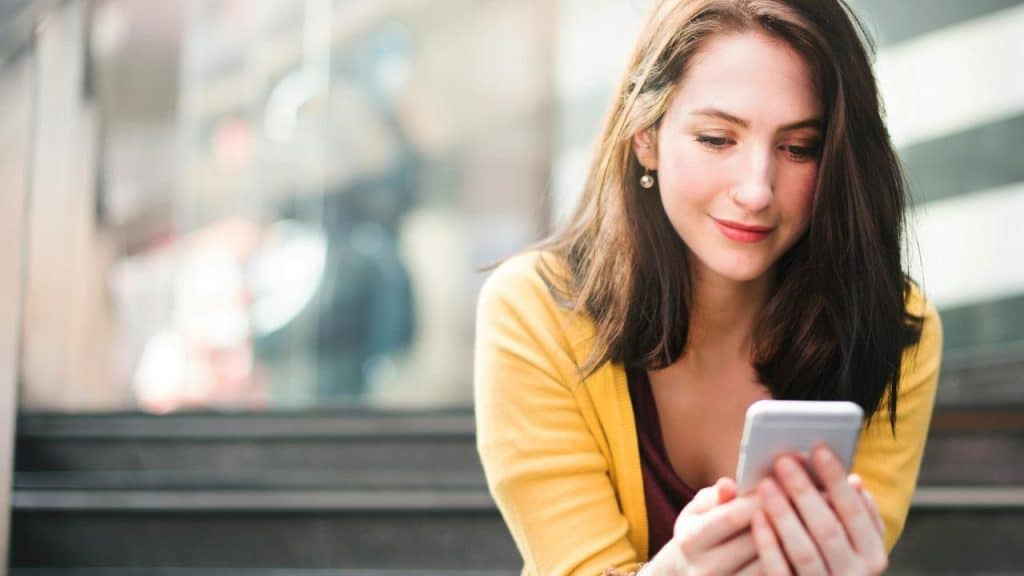 A woman in a yellow cardigan looking at her smartphone indoors.