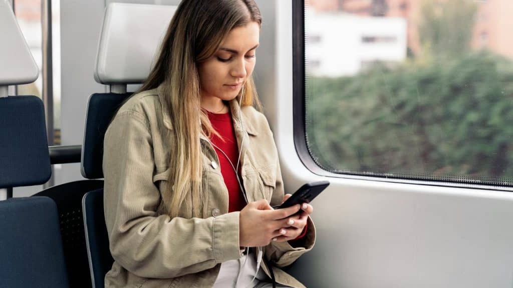 A woman seated on a train looking at her smartphone by a window.