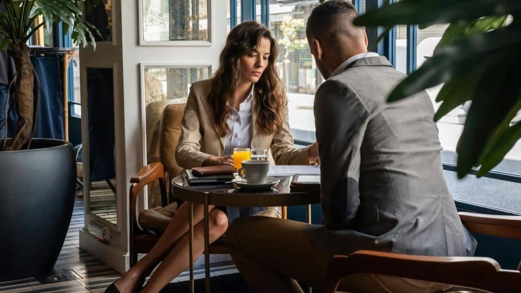 A man and woman sitting at a café table, reviewing documents over coffee.