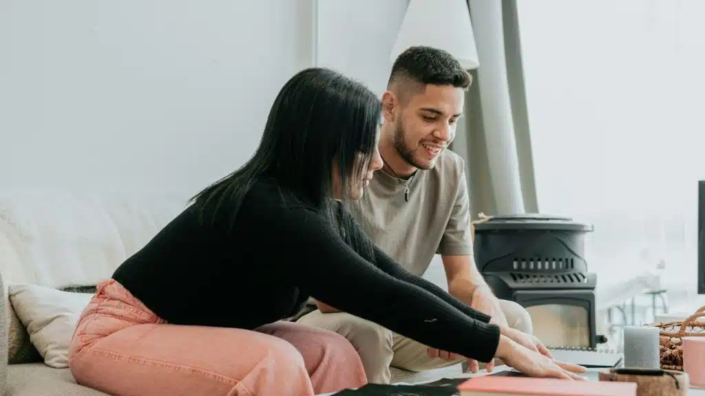 A couple sitting together on a couch, looking at papers in a bright living room.
