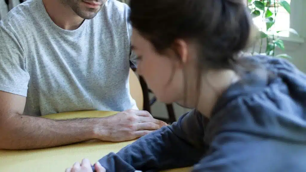 A man and a woman sitting close together at a table indoors, focused on their hands.