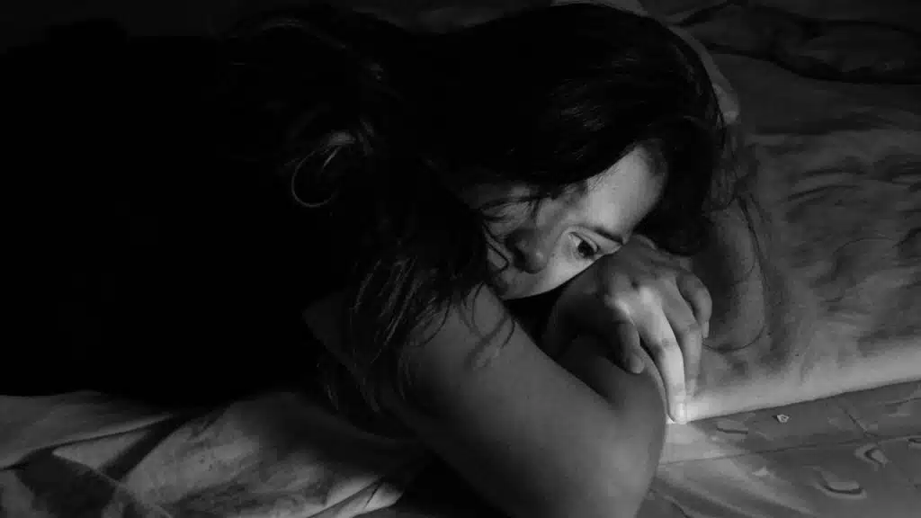 A woman lying on a bed in black and white, resting her head on her arm.