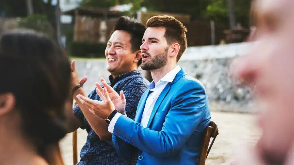 A group of men applauding while seated outdoors at an event.