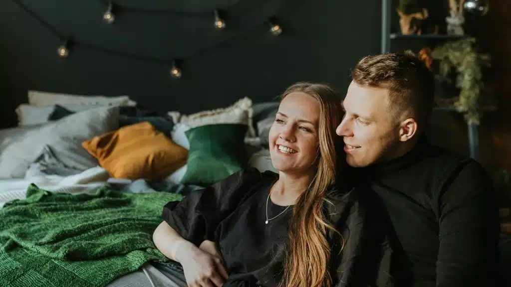A couple relaxing together on a bed in a cozy, softly lit bedroom.