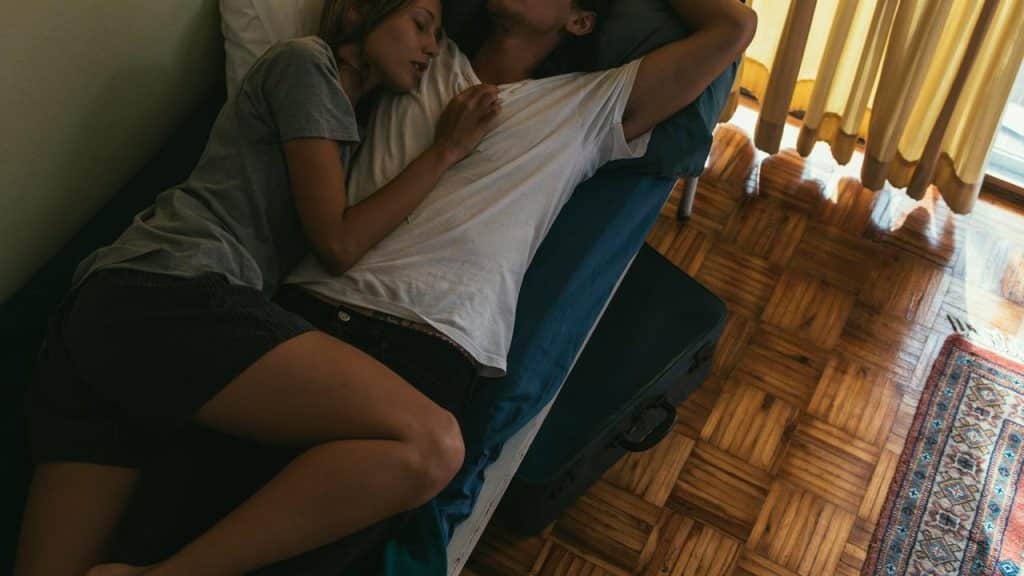 A couple cuddling and resting together on a bed in soft light.