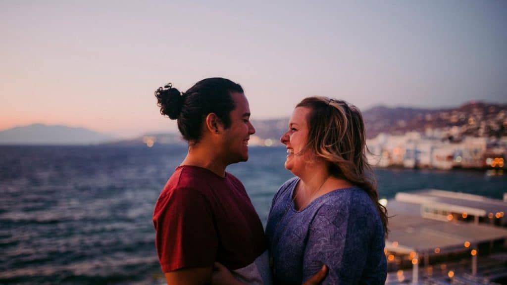 A couple smiling at each other by the ocean at sunset.