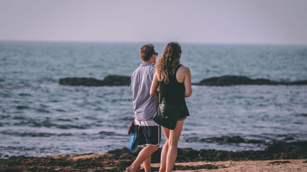 A couple standing on a rocky shore, looking out at the ocean.
