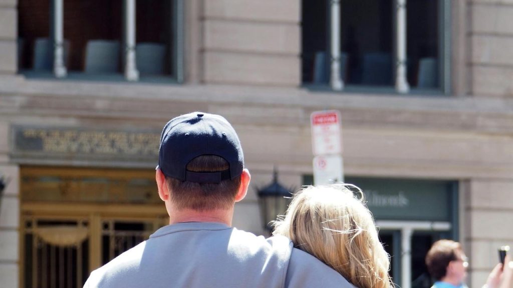 A couple seen from behind with one person’s arm around the other on a city street.