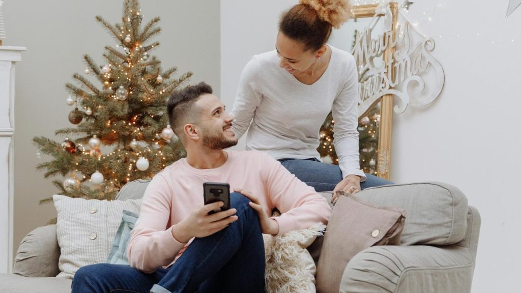 A couple smiling together on a couch near a decorated Christmas tree.